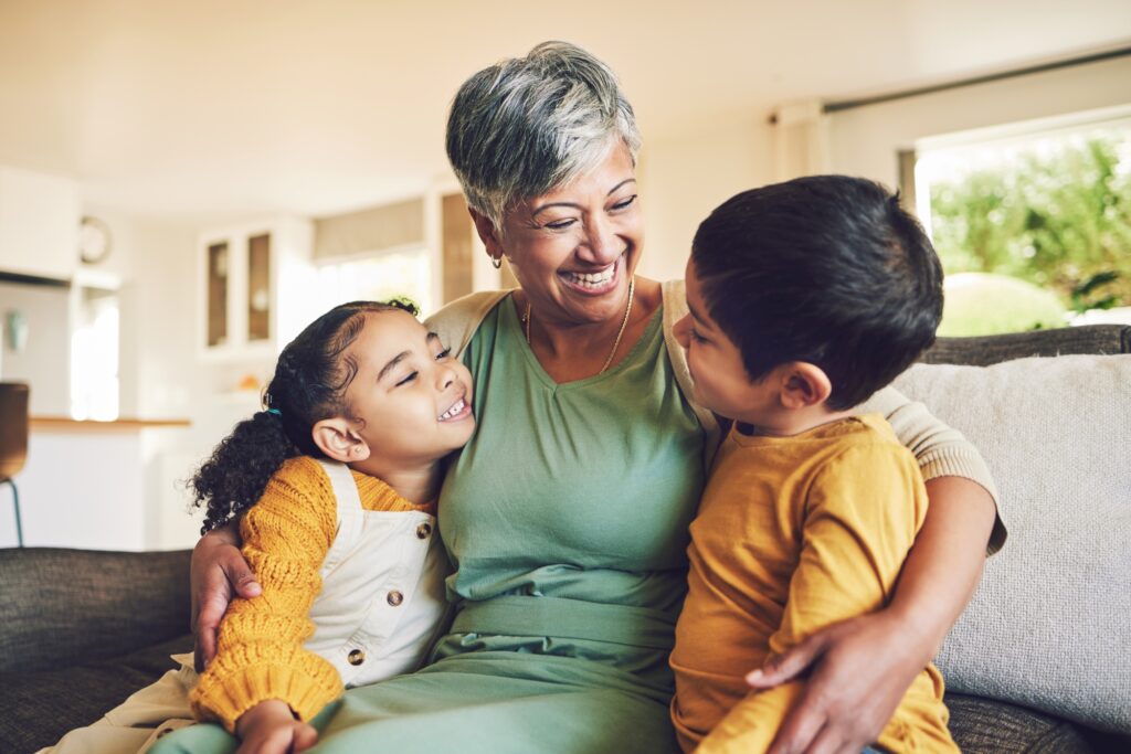 Smiling grandmother sits on a couch hugging two young grandchildren in a bright living room, representing family legacy planning and the MA estate tax exemption.